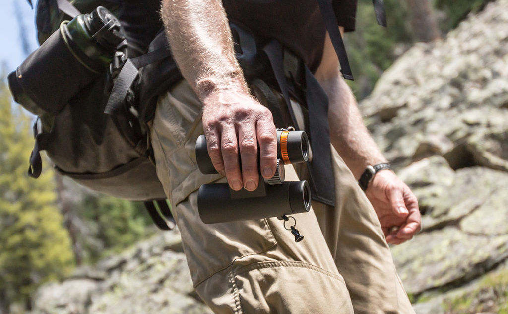 Someone holding a pair of Maven binoculars down by their side.
